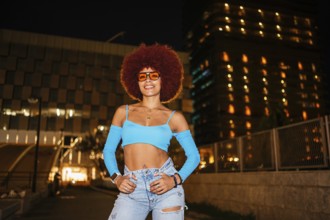 African descendent woman with striking afro hair and sunglasses poses confidently outdoors at night