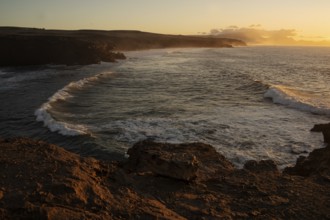 Dramatic view of powerful waves hitting rugged rocks with a sunset backdrop at La Pared,