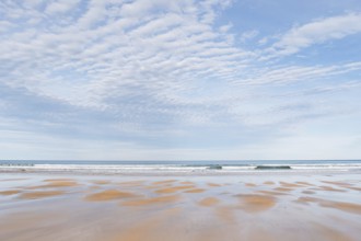 A tranquil beach scene featuring an expansive view of gentle waves under a sky filled with soft