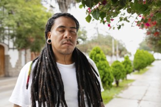 A man with long dreadlocks stands peacefully with his eyes closed under blooming bougainvillea