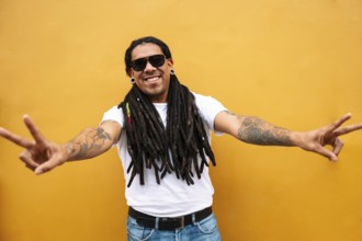 A cheerful man with long dreadlocks and tattoos poses against a vibrant yellow wall in Barranco,