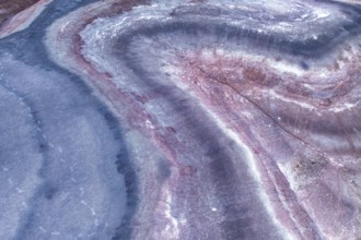 Close up of an sandstone surface, showcasing wavy patterns in pink and blue hues. The intricate