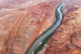 Aerial shot displays the meandering Rio San Juan snaking through vibrant red, rocky terrains of
