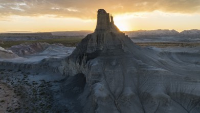 A breathtaking view of the sun setting behind a towering rock formation in Utah, casting a warm
