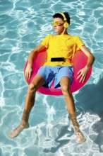 A young teenage boy in vibrant summer attire floats on a pink inflatable ring in clear blue pool