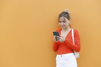 A woman in a vibrant orange outfit uses her smartphone against a matching orange background in