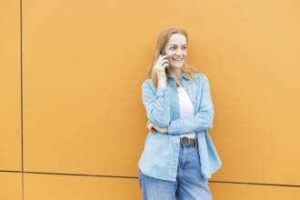 A woman in casual blue and white attire stands against a bright orange wall in Warsaw, Poland,