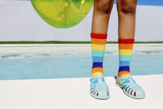 Vibrant rainbow socks and turquoise sandals by a pool, capturing summer's essence. The bright