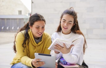 Two students sit together outdoors, enjoying a collaborative study session One holds a tablet,