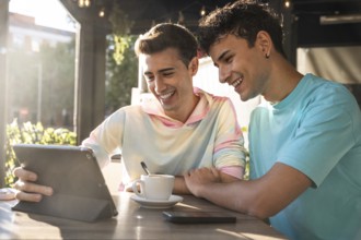 A joyful gay couple shares a moment at a sunny cafe, enjoying coffee and exploring content on a