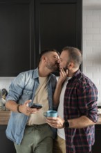 A loving gay couple shares a tender kiss in their kitchen, creating a warm and intimate atmosphere.