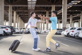 A cheerful gay couple reunites in a spacious parking lot, one carrying a suitcase. They are