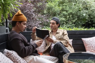 A Colombian gay couple enjoys a quiet day outdoors on a cozy bench. One reads from a book, while