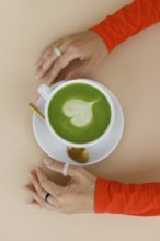 A woman enjoys a matcha latte in a Warsaw cafe Her vibrant orange clothing and trendy rings add