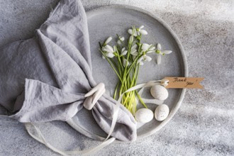 Top view of an exquisite spring table setting featuring fresh snowdrops arranged on a gray ceramic