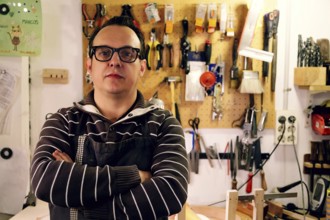 A luthier stands confidently in a bass guitar workshop, surrounded by tools and equipment. The