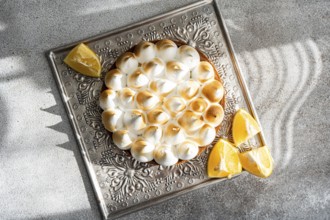 Top view of a homemade lemon cake on a decorative tray surrounded by lemon wedges. The dessert is