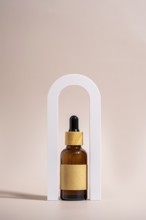 An amber glass dropper bottle with a wooden cap and blank label is elegantly placed in a white arch