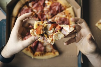 From above cropped unrecognizable close-up of a person's hands holding a piece of pepperoni and