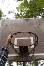 A hand reaches up to grab an old, iron basketball hoop with a chain net in an outdoor area
