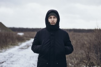 A man walks down a snowy path, dressed warmly in a coat and beanie, enjoying the serene winter