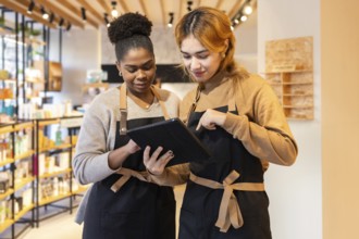 Two employees in a cosmetics store wearing aprons collaborate on a digital tablet, discussing