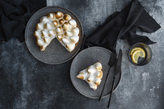 A delectable homemade lemon cake with toasted meringue, served on gray plates. Black cutlery and a