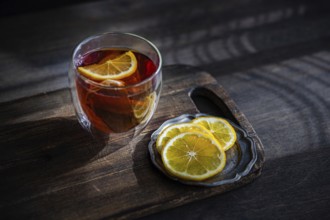 A cozy setting features a glass of rich, aromatic English tea with vibrant lemon slices, placed on