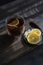 A clear glass filled with amber-colored tea accompanied by fresh lemon slices, set against a rustic