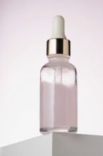 An elegant dropper bottle for cosmetics prominently displayed on a two toned minimalist podium,