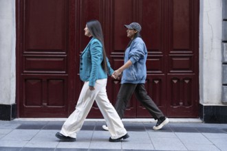 A Latin lesbian couple walks hand in hand along a city street. Their casual attire reflects modern
