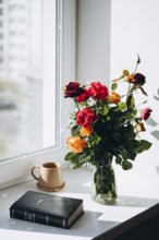 A serene windowsill featuring a bouquet of vibrant roses in a glass vase, a Bible, and a warm-toned