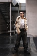 Fashionable woman wearing a trendy fur jacket, sunglasses, and wide-leg pants stands confidently in