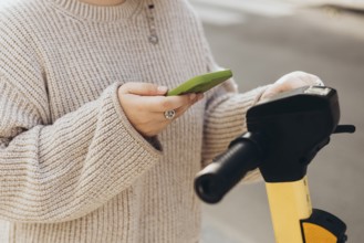 Cropped unrecognizable woman scans QR code with a smartphone to rent an electric scooter. The focus