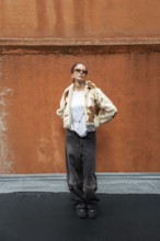 Stylish woman posing in a trendy fur jacket and sunglasses, set against a textured orange wall. The