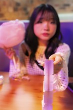An Asian Gen Z girl delights in the arcade atmosphere, holding cotton candy while playing a game