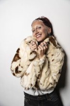 A woman with short hair smiles warmly at camera while wearing a fashionable faux fur jacket