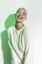 A cheerful middle-aged woman with a shaved head smiles brightly. She wears a textured white