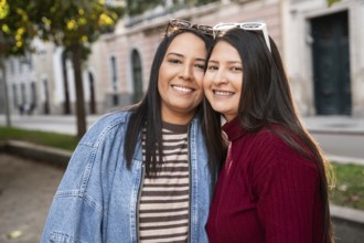 Portrait of a joyful Latin lesbian couple looking at camera against city background on a sunny day