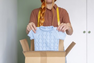 A woman is organizing her closet, preparing clothes for online sale. She holds a blue knit sweater
