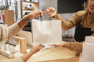 A customer receives a shopping bag from a worker at a cosmetics store. The hands exchange