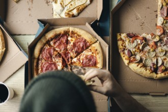 Cropped unrecognizable person taking a slice of pepperoni pizza from a box, accompanied by friends