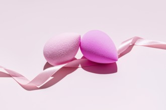 Two pink makeup sponges, also known as beauty blenders, intertwined with a soft pink ribbon, set