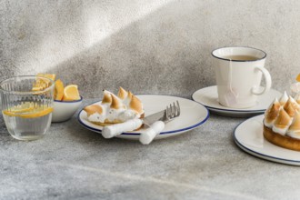 An elegant table setting with lemon meringue tarts, a cup of tea, and fresh lemon slices. Ideal for