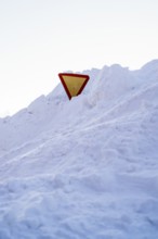 A yield sign partially buried in snow, standing amidst a snowy landscape in Swedish Lapland. The