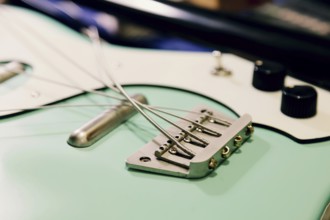Close-up of a bass guitar bridge and strings in a luthier workshop. The focus is on the intricate