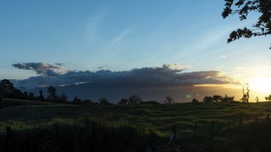 Capture the serene beauty of sunset over lush green fields under a vibrant sky lit by the