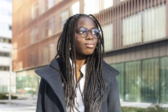 An African American businesswoman with braids and glasses takes a break outside a modern office