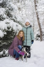 A joyful family poses with a dog in a snowy forest, surrounded by snow-covered trees. The bright