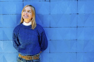 A cheerful woman smiles broadly while dressed in a blue checkered shirt and leaning against a
